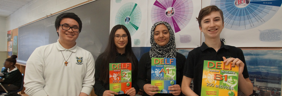 Two male and two female students in a classroom holding DELF books